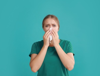 Young woman suffering from allergy on turquoise background