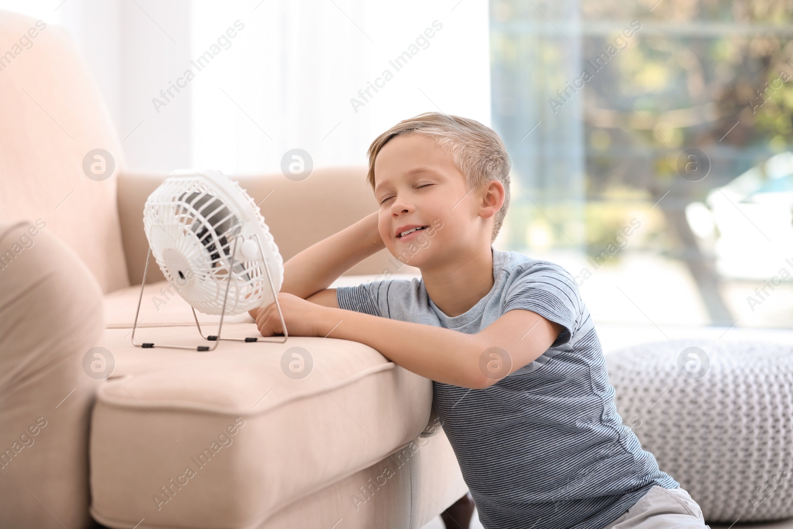 Photo of Little boy relaxing in front of fan at home. Summer heat