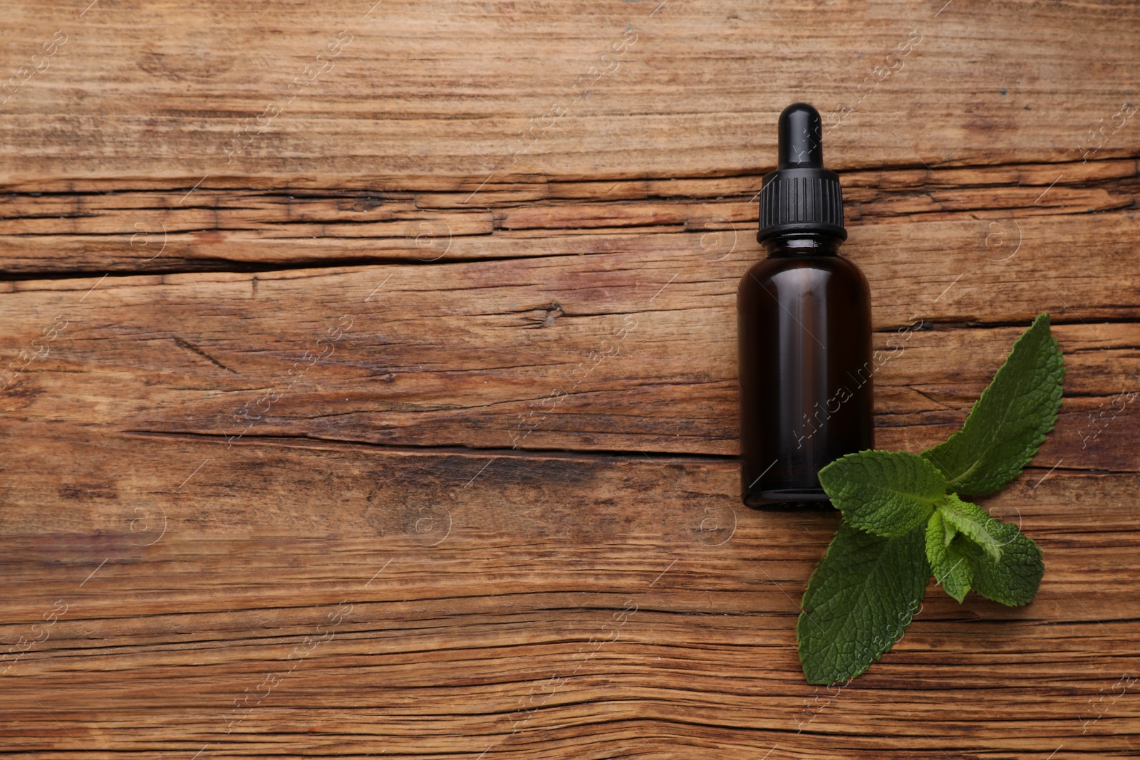 Photo of Bottle of essential oil and mint on wooden table, flat lay. Space for text