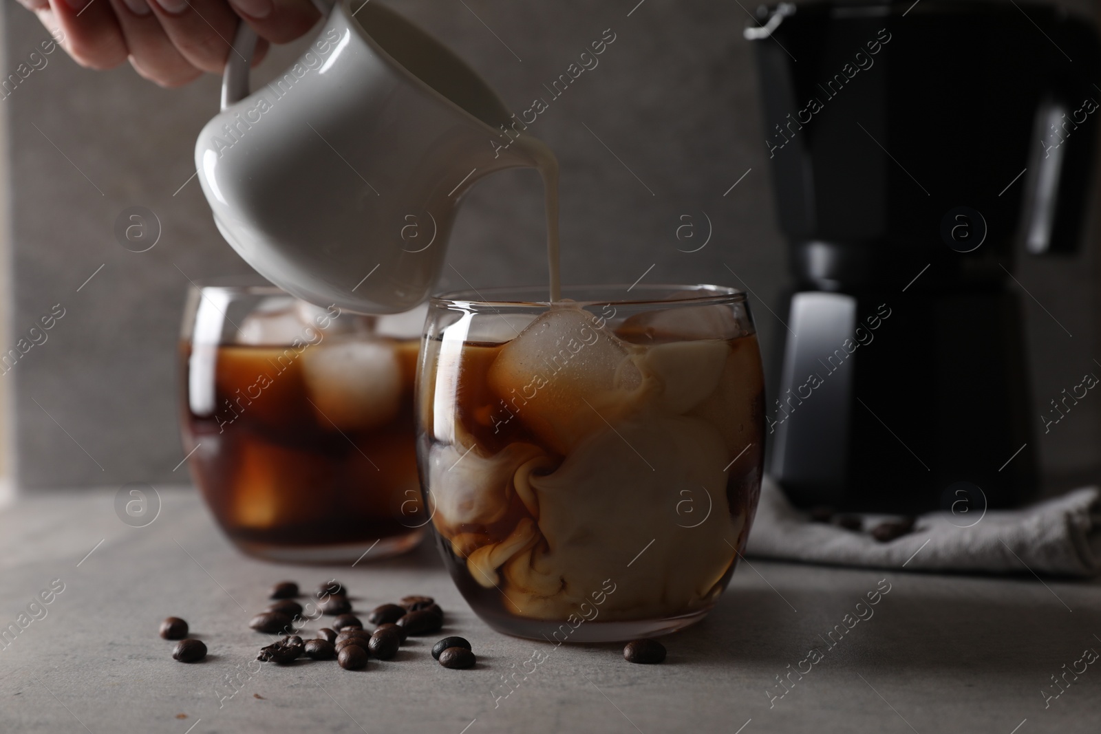 Photo of Woman pouring milk into glass with refreshing iced coffee at gray table, closeup