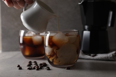 Photo of Woman pouring milk into glass with refreshing iced coffee at gray table, closeup