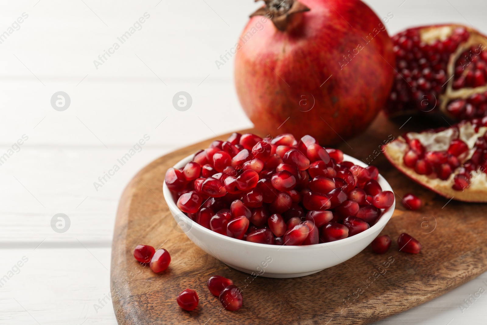 Photo of Ripe juicy pomegranate grains on white wooden table, space for text