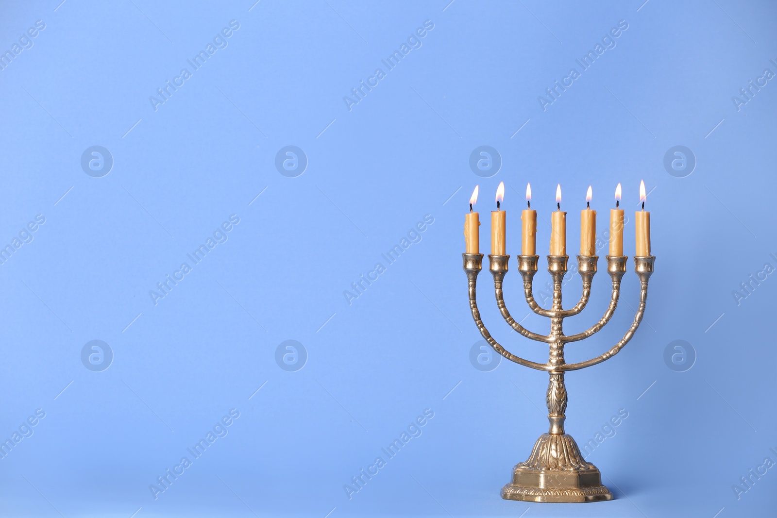 Photo of Golden menorah with burning candles on light blue background, space for text