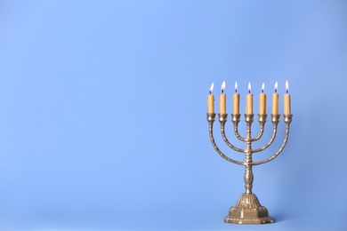 Photo of Golden menorah with burning candles on light blue background, space for text