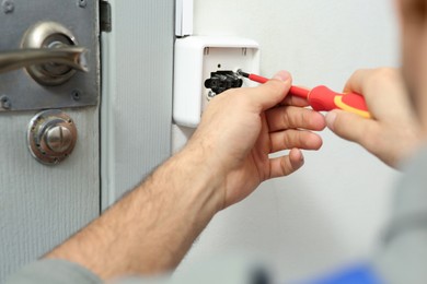 Professional electrician with screwdriver repairing light switch, closeup