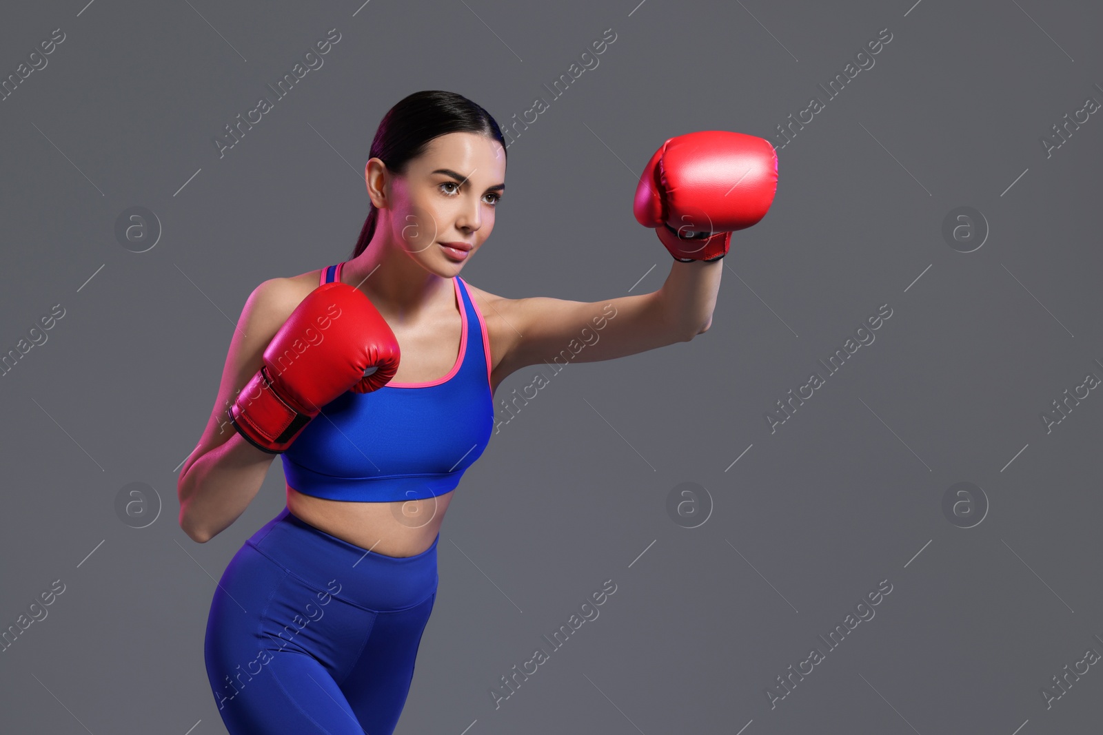 Photo of Beautiful woman wearing boxing gloves training in color lights on grey background