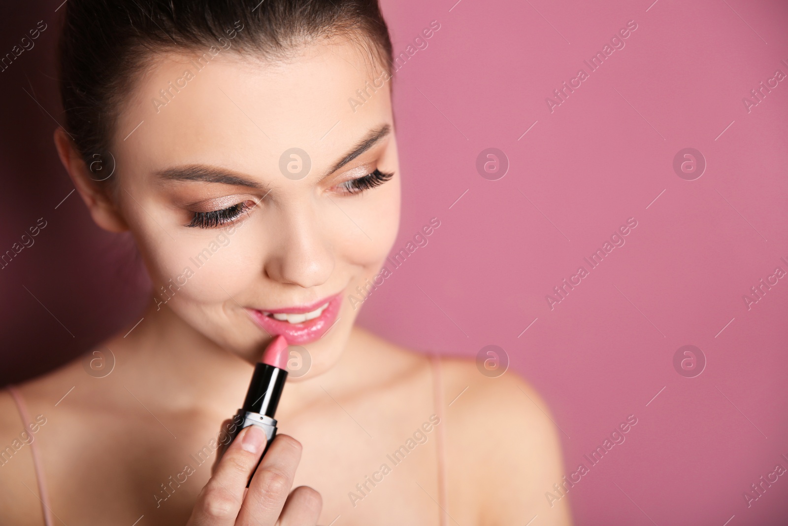 Photo of Young woman applying lipstick on color background. Professional makeup products