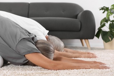 Photo of Senior couple practicing yoga on carpet at home. Healthy lifestyle