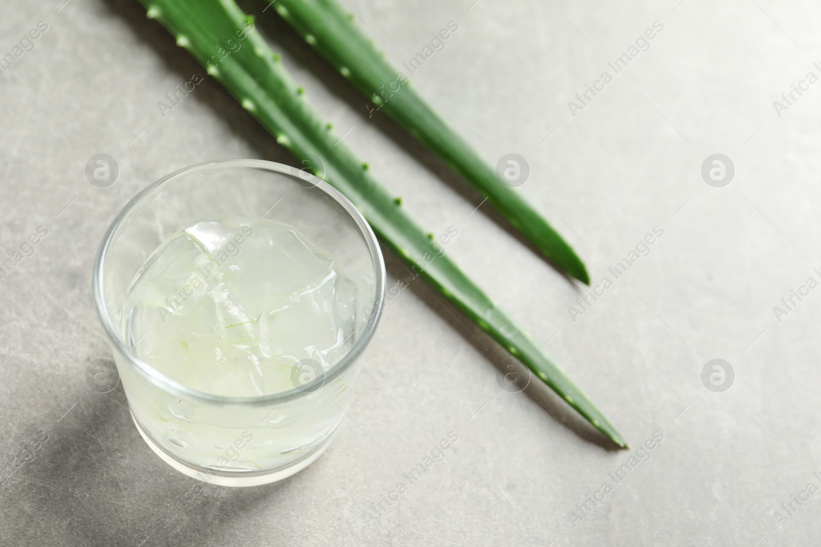 Photo of Glass with peeled aloe vera and green leaves on gray table. Space for text