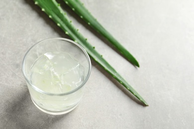 Photo of Glass with peeled aloe vera and green leaves on gray table. Space for text