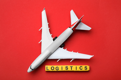 Photo of Flat lay composition with toy plane and word LOGISTICS on red background. Wholesale concept