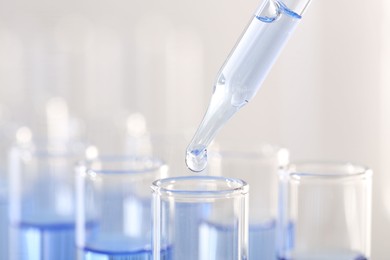 Laboratory analysis. Dripping light blue liquid from pipette into glass test tube on blurred background, closeup