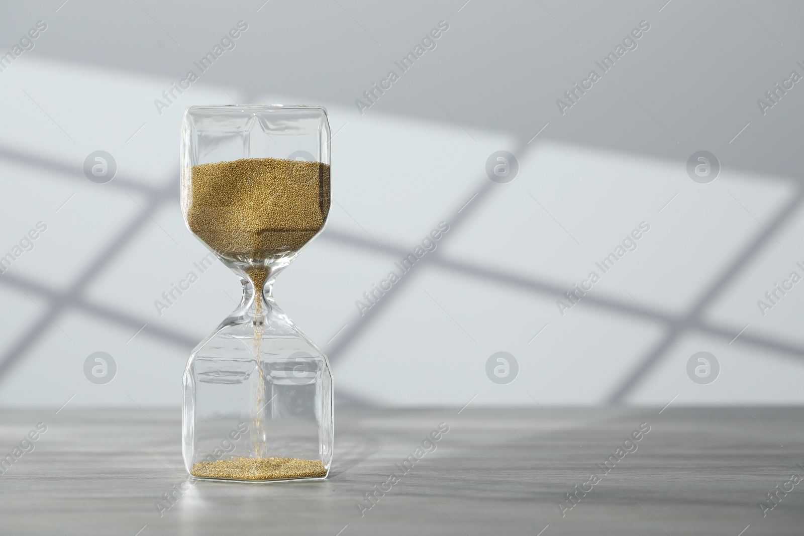 Photo of Hourglass with flowing gold sand on table against white wall, space for text