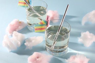 Photo of Tasty cocktails in glasses decorated with gummy candies and cotton candy on light blue background
