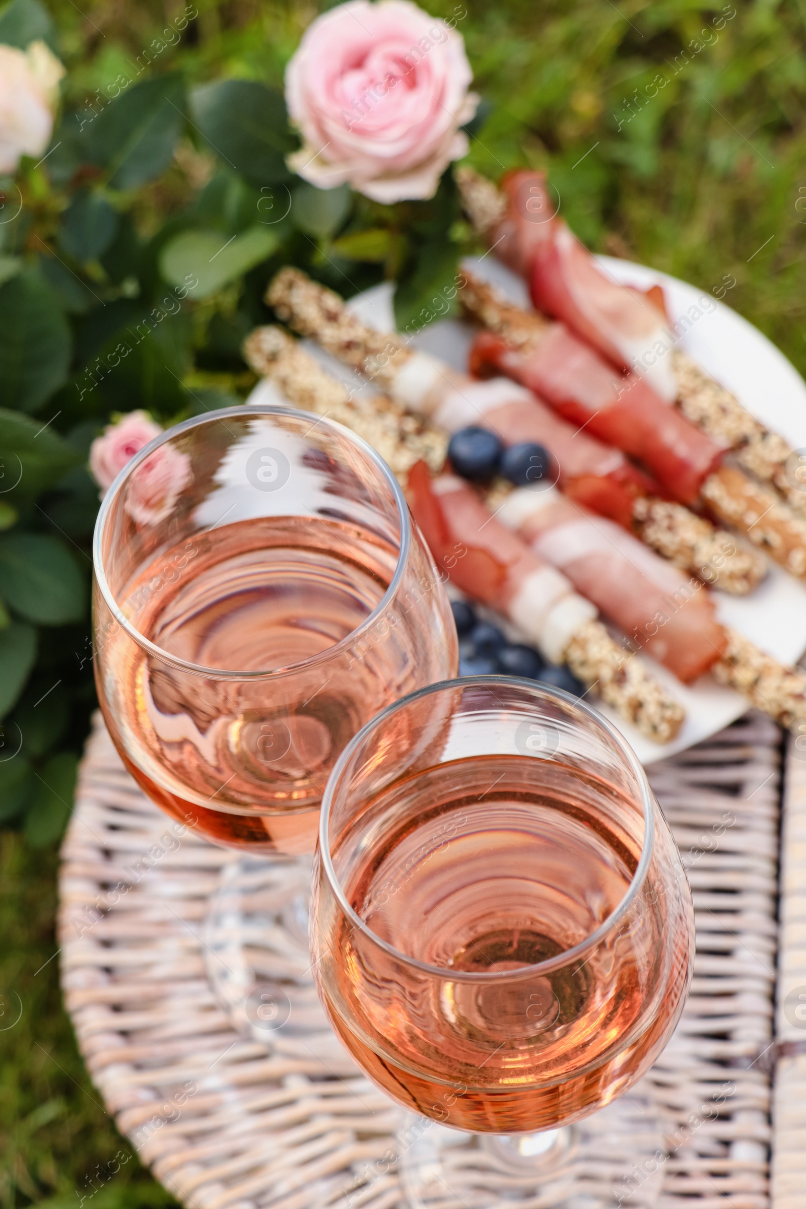 Photo of Glasses of delicious rose wine and food on picnic basket outdoors, closeup