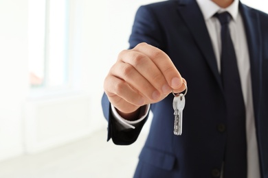 Photo of Real estate agent holding keys on blurred background, closeup