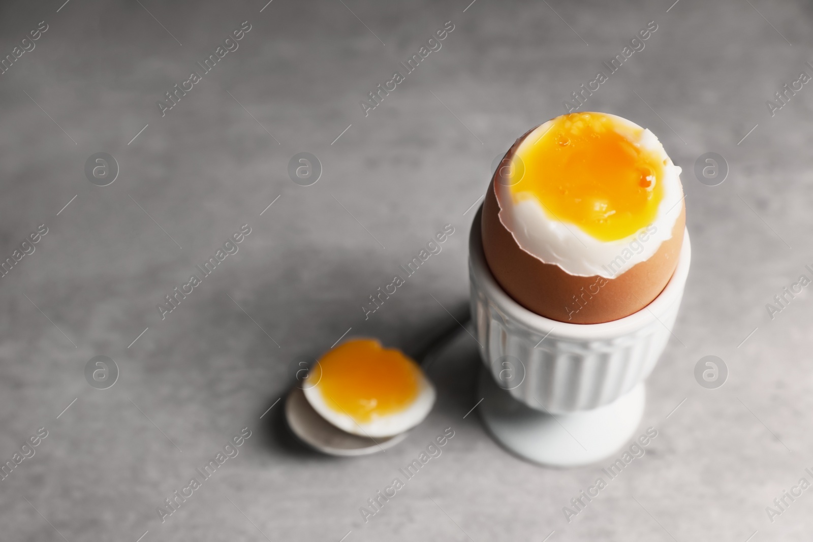 Photo of Fresh soft boiled egg in cup on grey table. Space for text