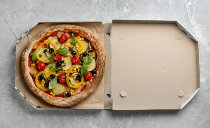 Tasty vegetable pizza in cardboard box on light grey table, top view