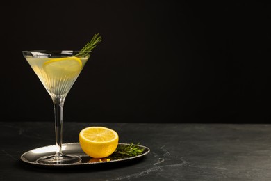 Photo of Martini glass of refreshing cocktail with lemon slice, rosemary and fresh fruit on black table, space for text