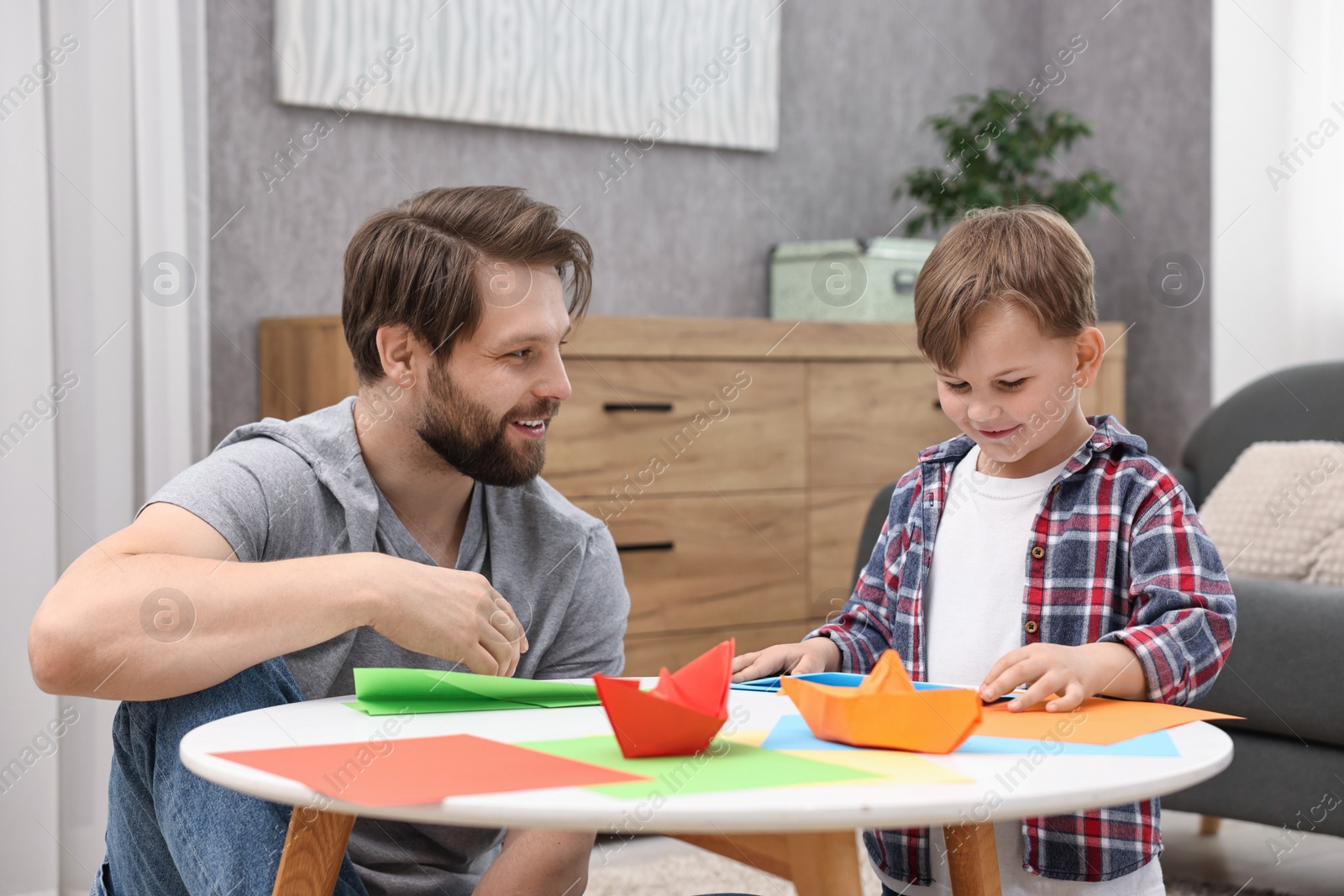 Photo of Dad and son making paper boats at coffee table indoors