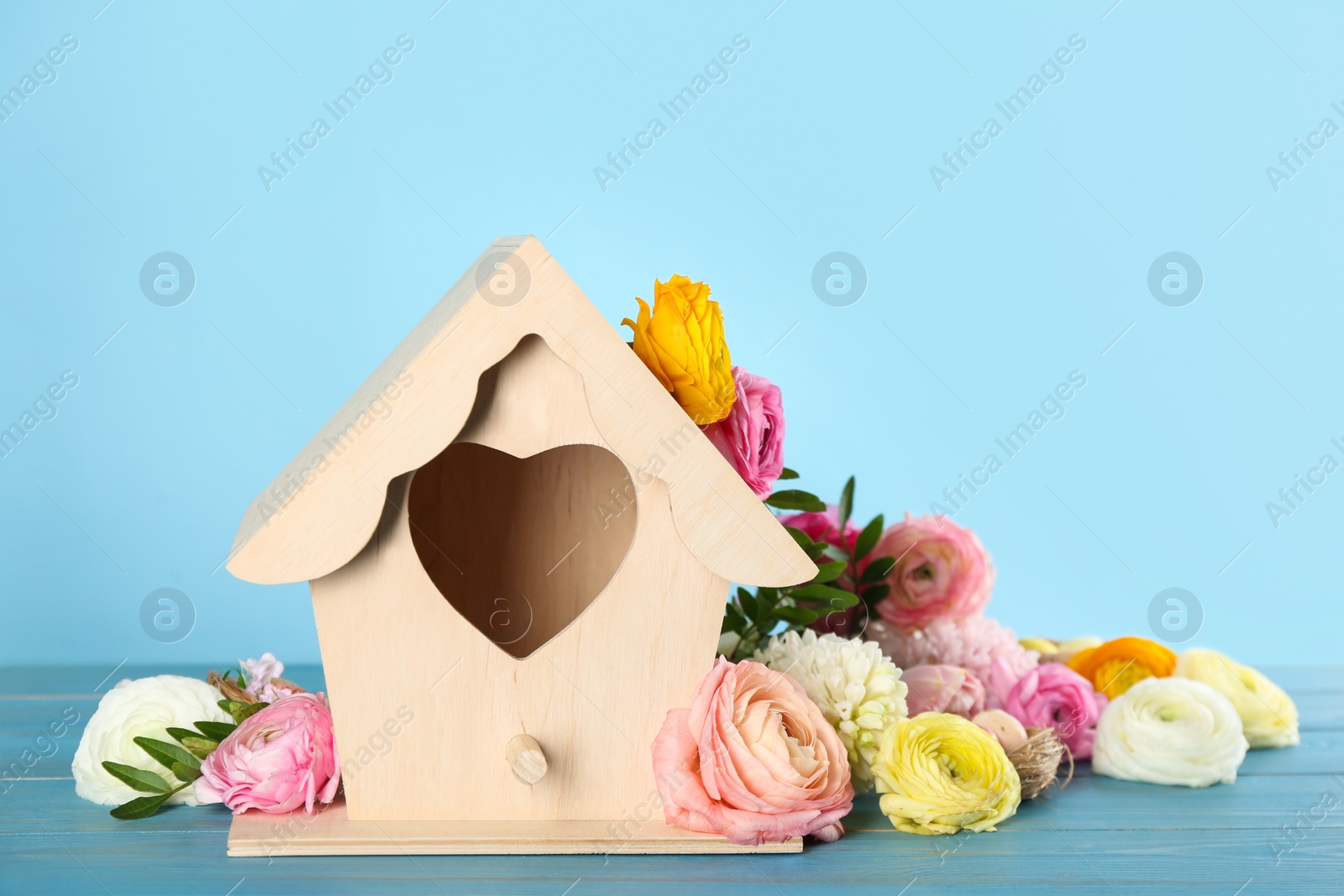 Photo of Stylish bird house and fresh eustomas on light blue wooden table