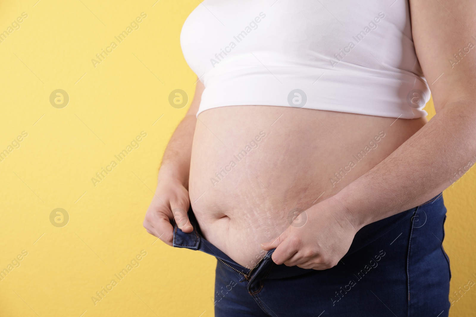 Photo of Overweight woman trying to wear tight jeans on color background, closeup. Space for text