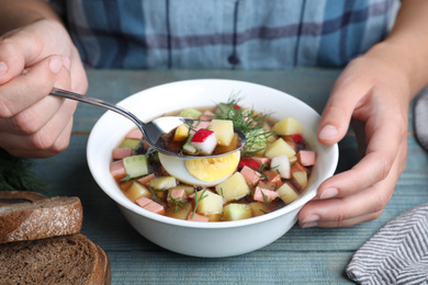 Photo of Woman eating delicious cold okroshka with kvass at blue wooden table, closeup. Traditional Russian summer soup