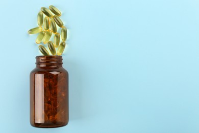 Photo of Bottle and vitamin capsules on light blue background, top view. Space for text