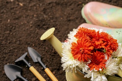 Photo of Gardening tools, boots and flowers on fresh soil, closeup. Space for text