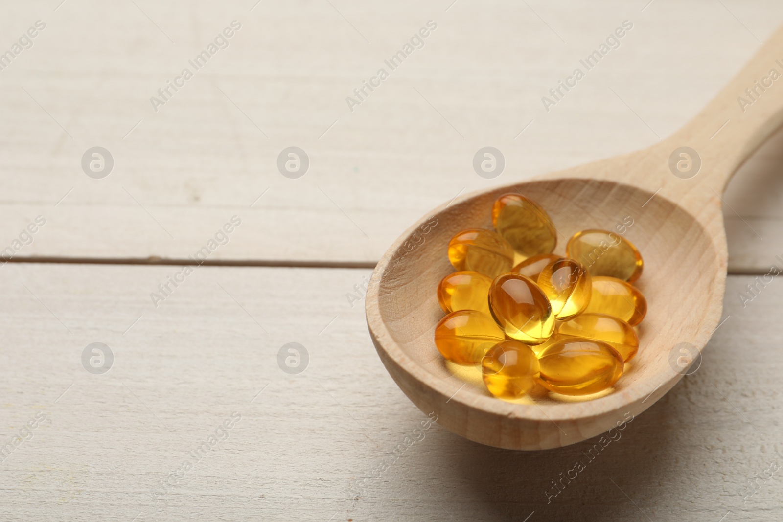 Photo of Spoon with dietary supplement capsules on white wooden table. Space for text