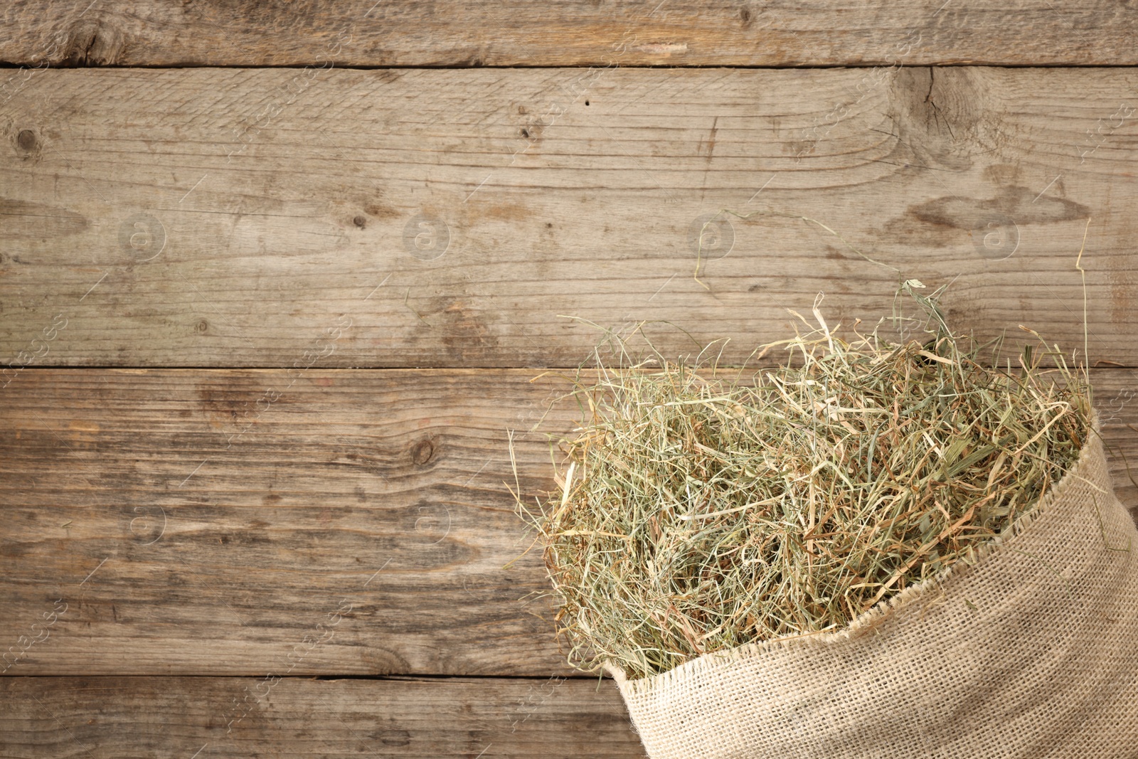 Photo of Burlap sack with dry herb on wooden table, top view. Space for text