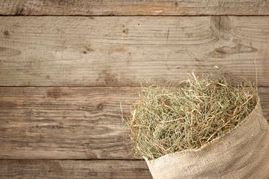 Burlap sack with dry herb on wooden table, top view. Space for text