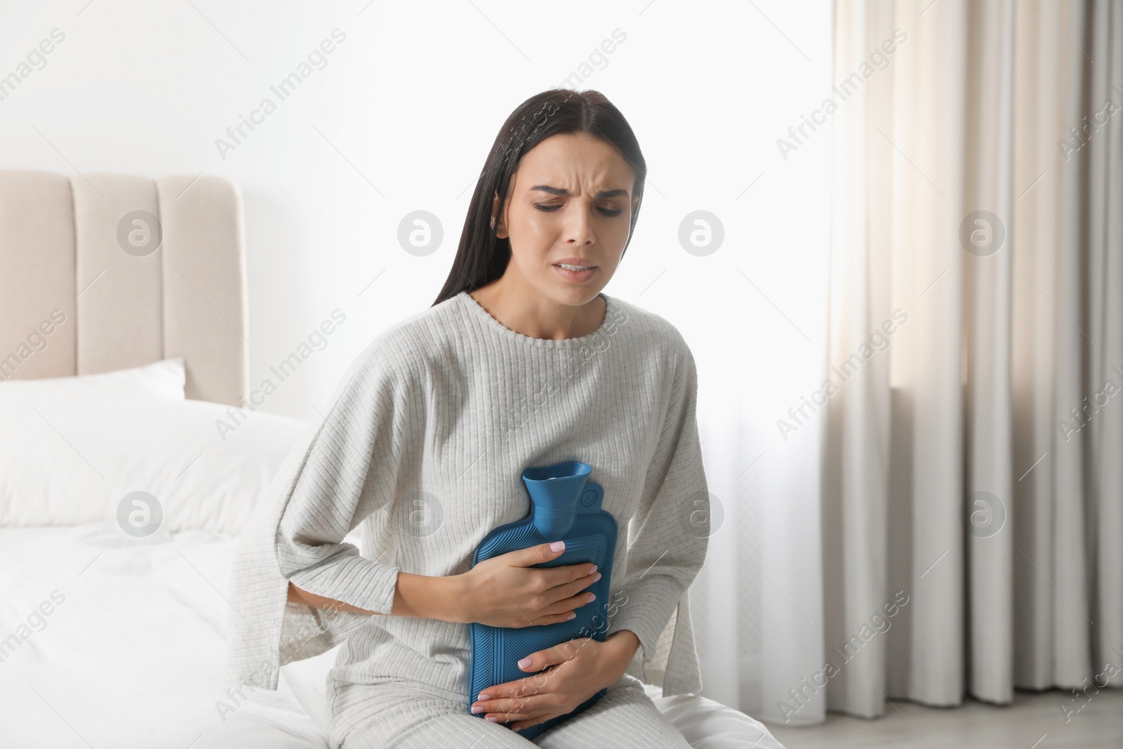 Photo of Woman using hot water bottle to relieve abdominal pain on bed at home