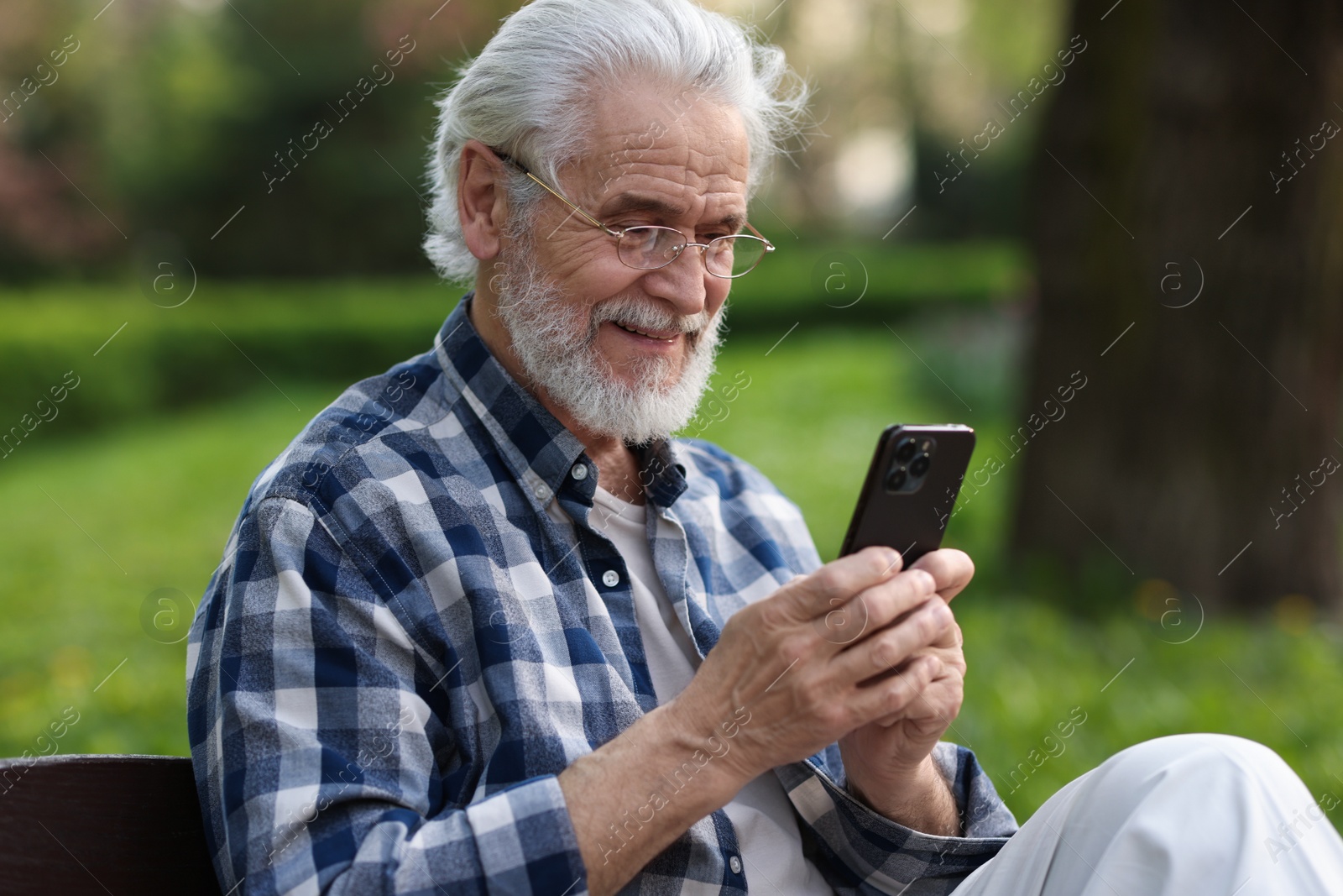 Photo of Portrait of happy grandpa with glasses using smartphone on bench in park