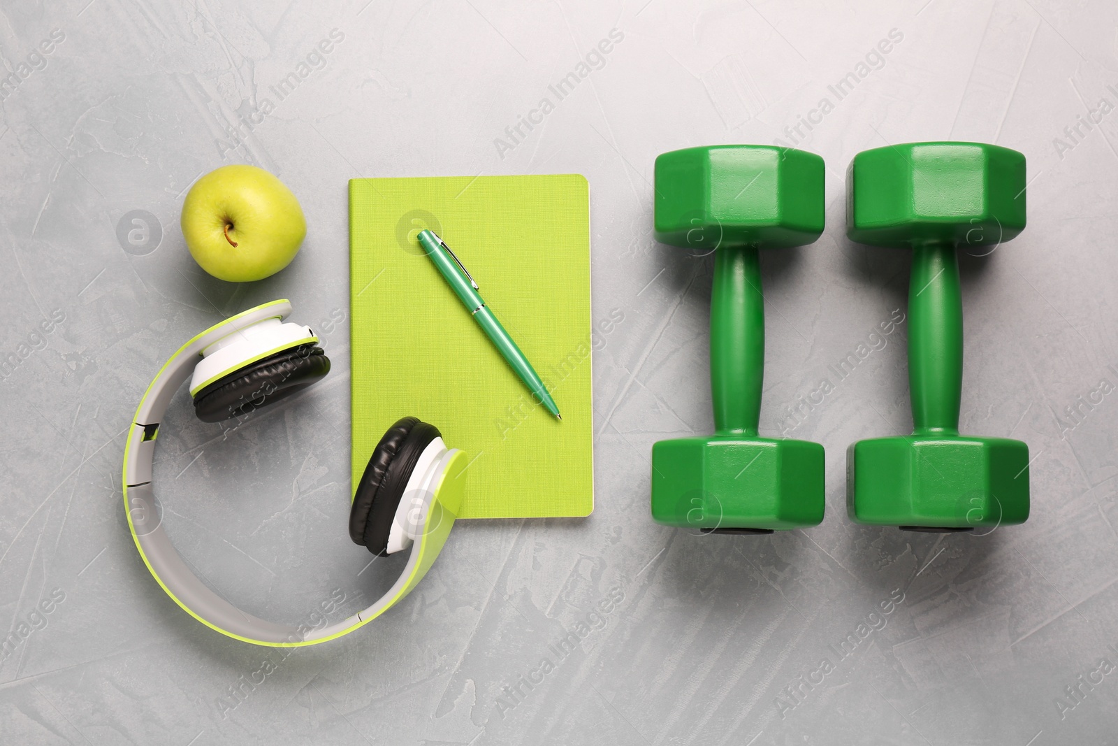 Photo of Dumbbells, headphones, apple and stationery on light grey table, flat lay