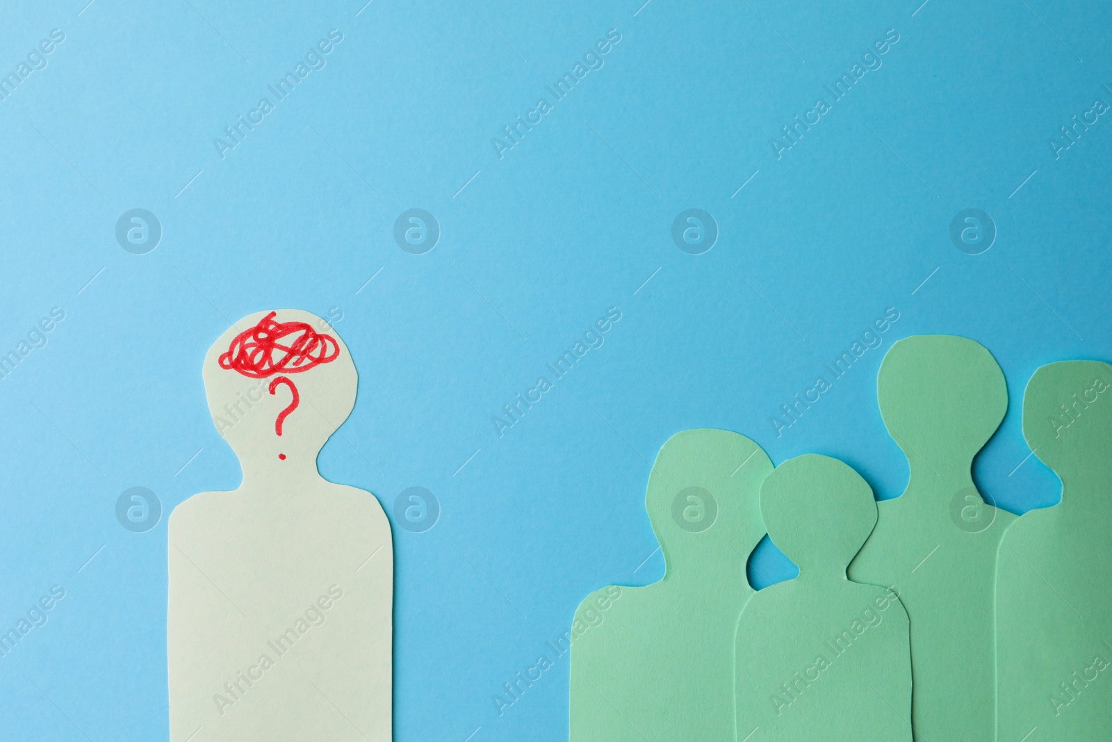 Photo of Paper cutout of crowd with one human silhouette different from others on light blue background, flat lay. Emotional management