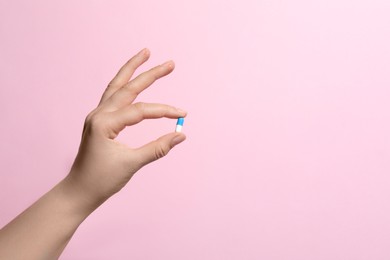 Woman holding pill on pink background, closeup. Space for text