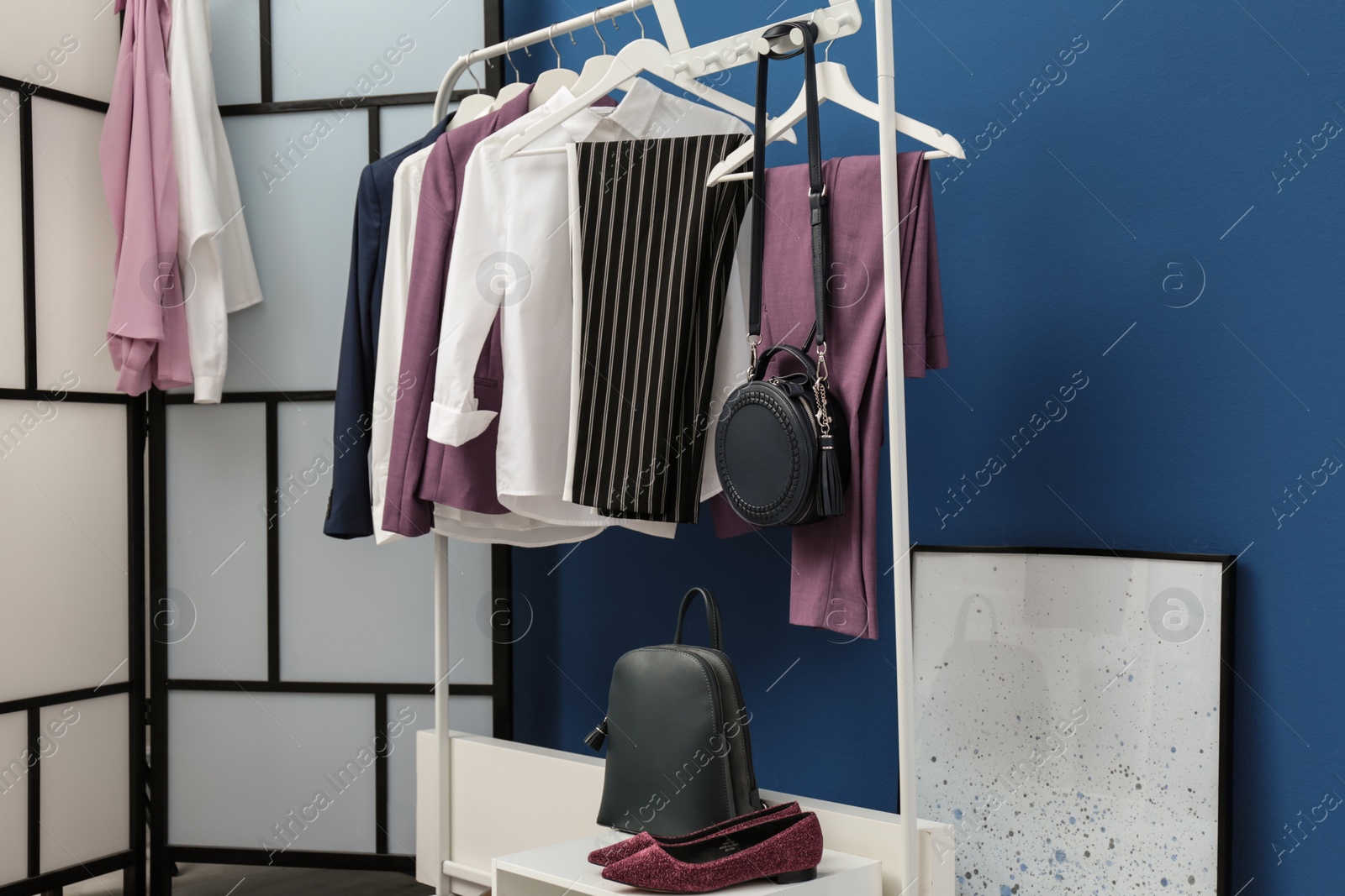 Photo of Wardrobe rack with women's clothes and shoes at blue wall in room