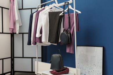 Wardrobe rack with women's clothes and shoes at blue wall in room