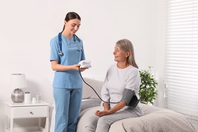 Young healthcare worker measuring senior woman's blood pressure indoors