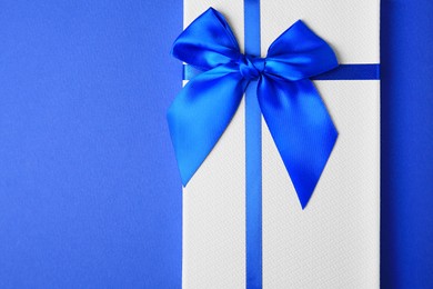Photo of Beautiful gift box with bow on blue background, top view. Space for text