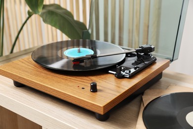 Photo of Stylish turntable with vinyl disc on light wooden table indoors