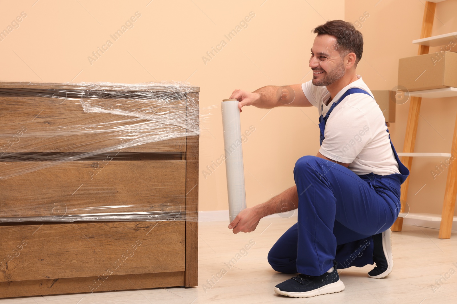 Photo of Workers wrapping chest of drawers in stretch film indoors