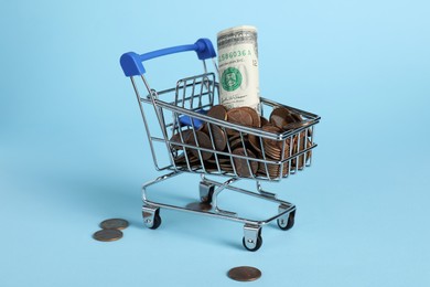 Small metal shopping carts with money on light blue background
