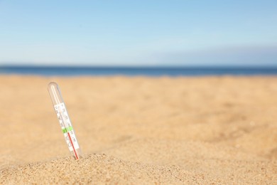 Weather thermometer in sand near sea, space for text