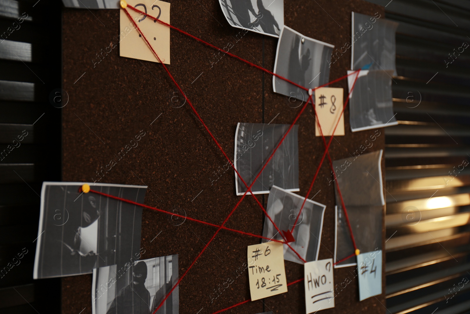 Photo of Detective board with crime scene photos, stickers, clues and red thread on wall, closeup