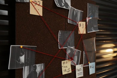 Detective board with crime scene photos, stickers, clues and red thread on wall, closeup