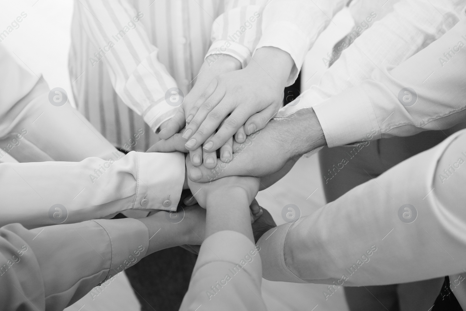 Image of People holding hands together in office, closeup. Black and white effect