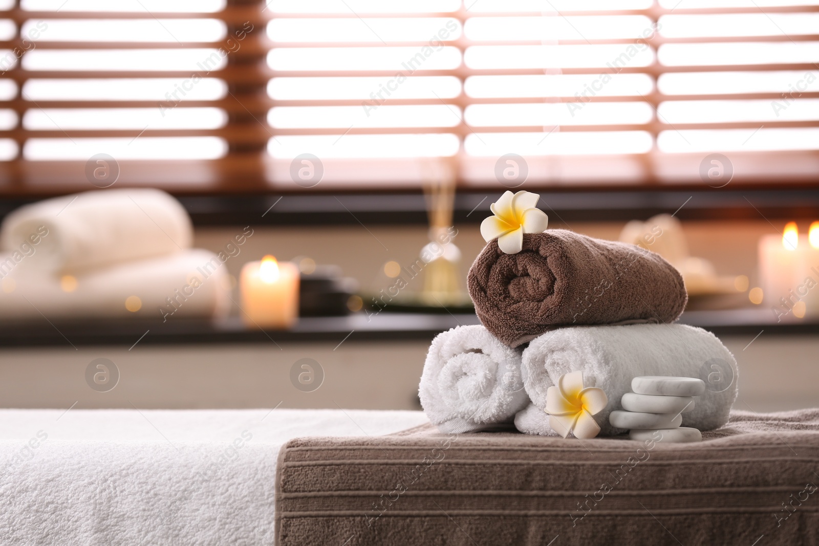 Photo of Composition with towels, flowers and stones on massage table in spa salon. Space for text