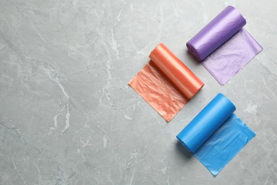Photo of Rolls of different color garbage bags on light grey marble table, flat lay. Space for text